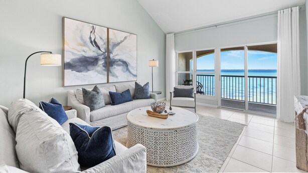 A modern living room with a large window overlooking the ocean, a round coffee table, and a sofa with blue cushions. - Carnoustie Sandestin Bayfront Condo Golf Cart (Miramar Beach)
