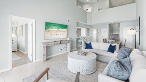 A spacious living area with a high ceiling, a fireplace, a round coffee table, and a large painting. - Carnoustie Sandestin Bayfront Condo Golf Cart (Miramar Beach)
