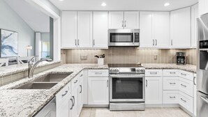 A modern kitchen with white cabinets, a stainless steel microwave, a built-in oven, and a granite countertop. - Carnoustie Sandestin Bayfront Condo Golf Cart (Miramar Beach)