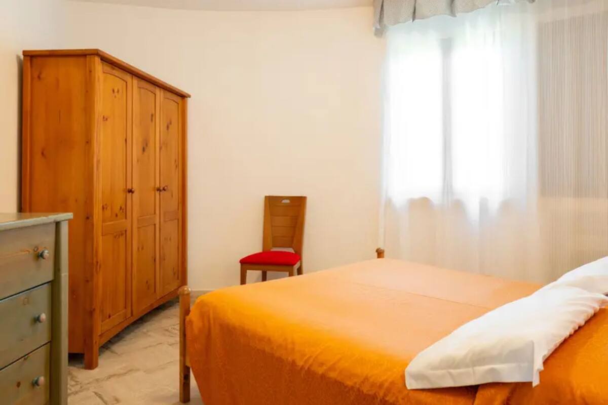 Een slaapkamer met een bed, een houten kledingkast, een stoel en een raam met gordijnen.
