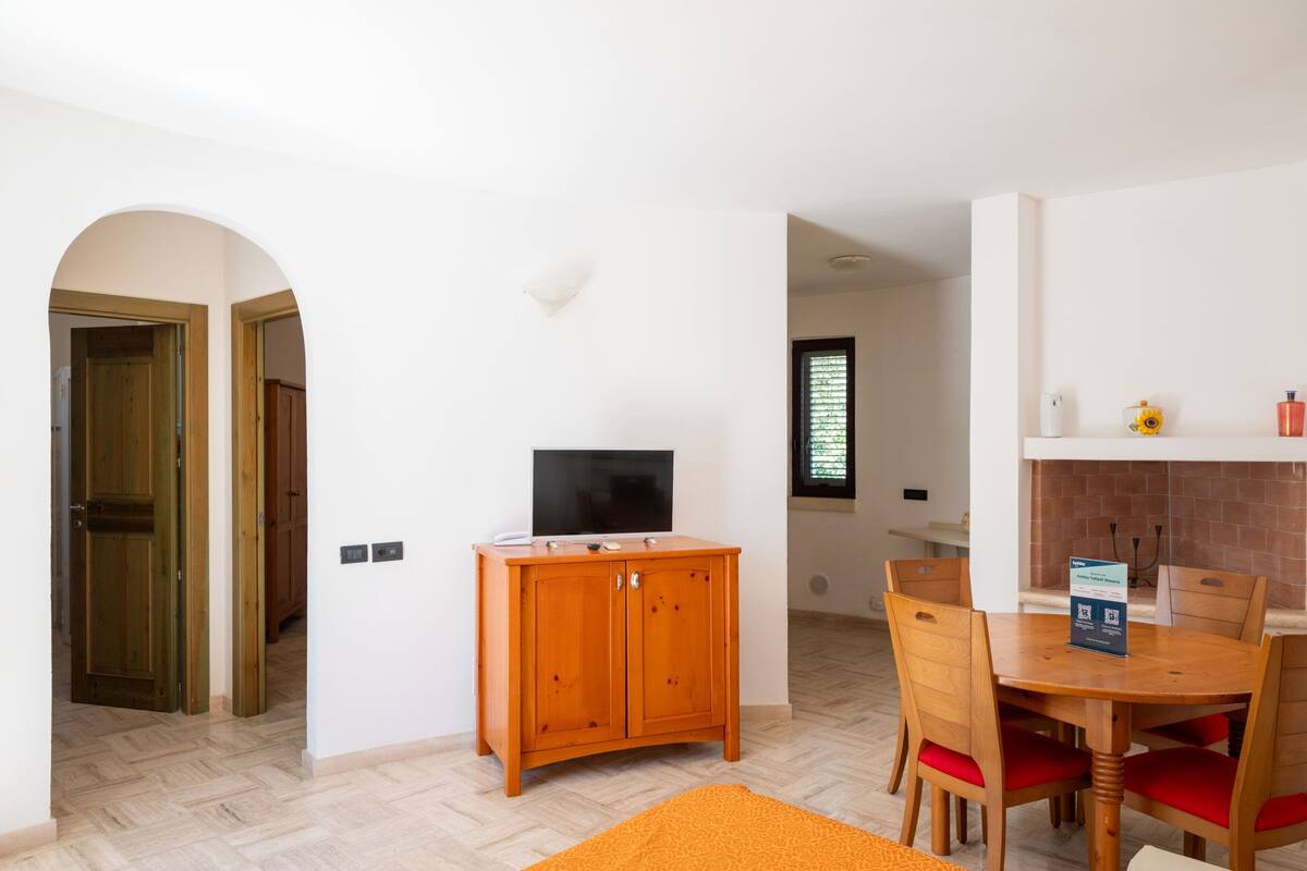 Een kamer met een houten kast, een televisie, een eettafel met stoelen en een open haard.