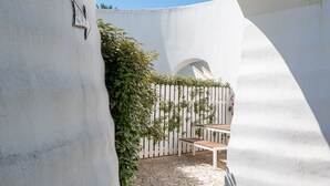 An arched doorway leading to a courtyard with a bench, a white wall, and a fence with greenery. - Hotiday Gallipoli Masseria (Tuglie)
