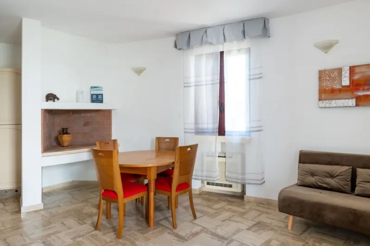 A dining area with a wooden table and chairs, a sofa, and a window with curtains.