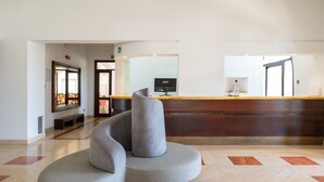 A reception area with a curved grey chair, a wooden reception desk, and a large mirror. - Hotiday Gallipoli Masseria (Tuglie)