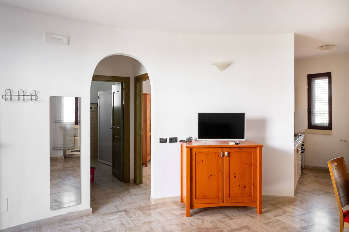 Een kamer met een houten kast, een flatscreen televisie, een rode stoel en een raam.