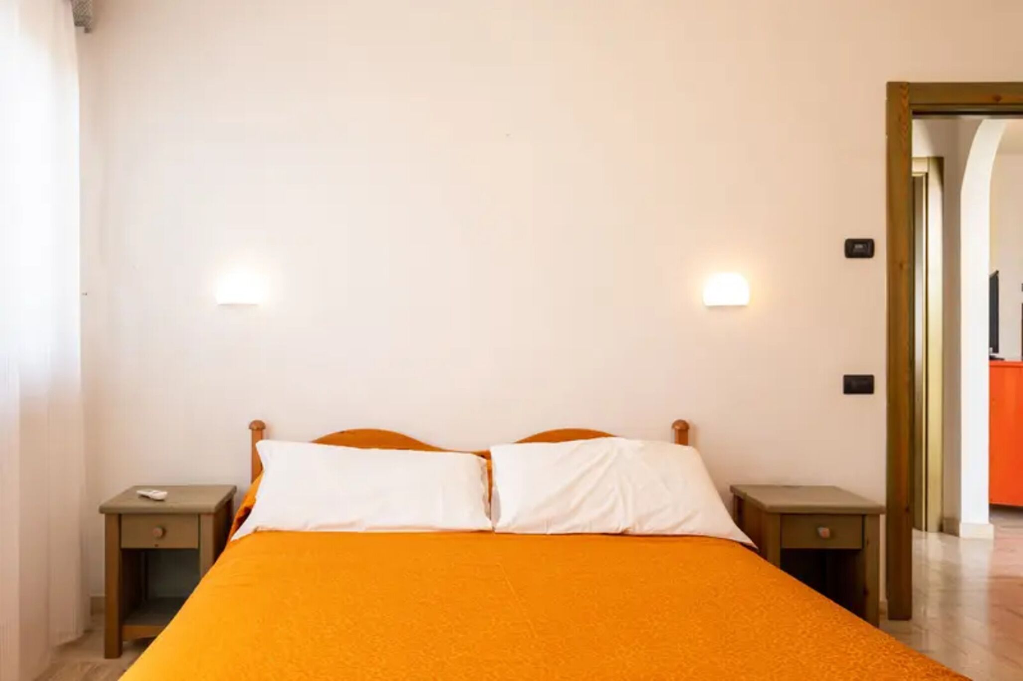 A single bed with an orange bedspread, two bedside tables, and two wall-mounted lights.