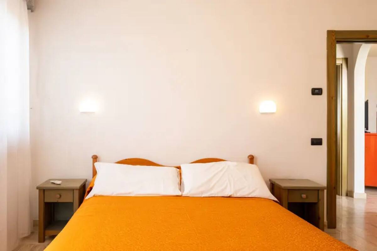 Een eenpersoonsbed met een oranje sprei, twee nachtkastjes en twee wandlampen.