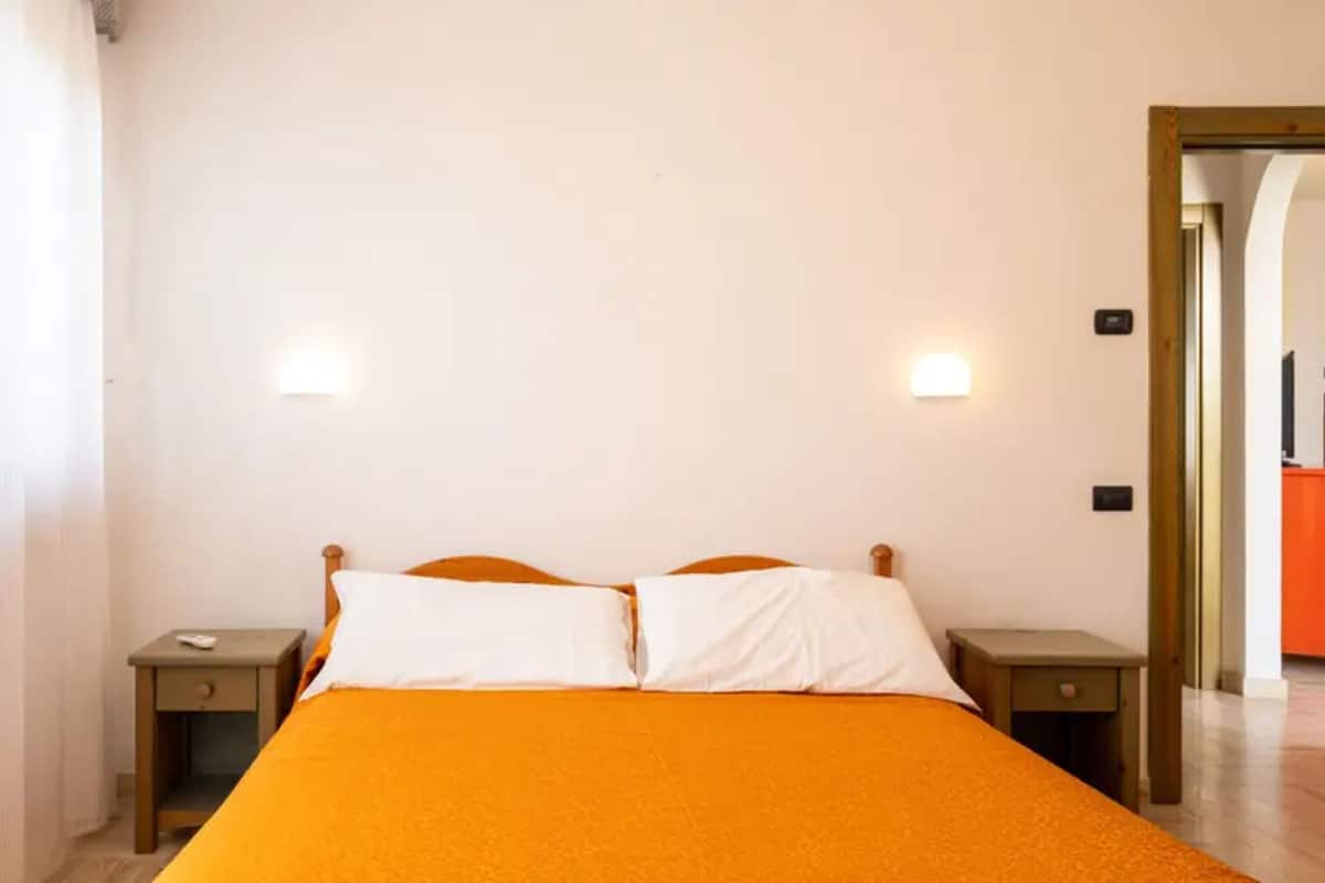A single bed with an orange bedspread, two bedside tables, and two wall-mounted lights.