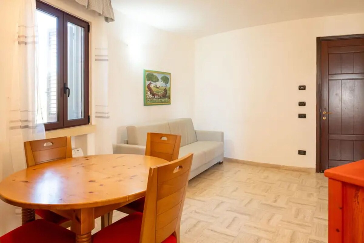 Una stanza con un tavolo da pranzo in legno, un divano, una porta e un quadro appeso al muro.