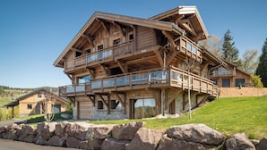 A multi-story wooden chalet with balconies, a stone foundation, and a surrounding stone wall. - Chalet Elixir - 14 guests - Pool & Sauna, Gérardmer (Gérardmer)