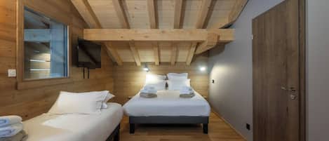 Una habitación con dos camas, vigas de madera en el techo, un televisor montado en la pared y una puerta de madera.