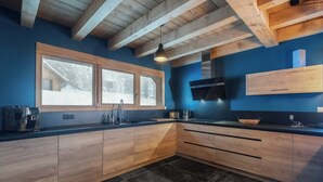 A modern kitchen with wooden cabinets, a black countertop, a window with a view of a snowy landscape, and a built-in microwave. - Chalet Elixir - 14 guests - Pool & Sauna, Gérardmer (Gérardmer)