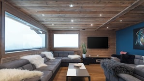 A modern living room with a sectional sofa, a coffee table, and a flat-screen TV mounted on a wooden wall. - Chalet Elixir - 14 guests - Pool & Sauna, Gérardmer (Gérardmer)