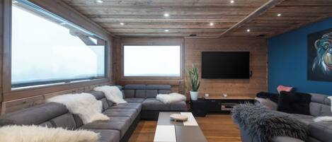 A modern living room with a sectional sofa, a coffee table, and a flat-screen TV mounted on a wooden wall.