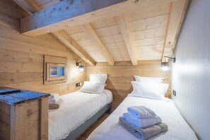 Una habitación de cabaña de madera con dos camas, un ventanal pequeño y un aparador de madera.