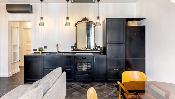 A modern kitchen with black cabinetry, a large mirror, pendant lights, and a built-in oven. - Genteel Home Belfiore (Florence)