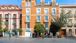 A row of colorful buildings with balconies, a clear sky, and pedestrians on the street. - Genteel Home San Fernando (Seville)