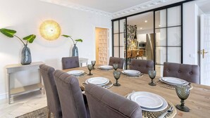A dining area with a wooden table set for six, surrounded by upholstered chairs. There are two large potted plants on the table, and a modern pendant light hangs above. - Genteel Home San Fernando (Seville)