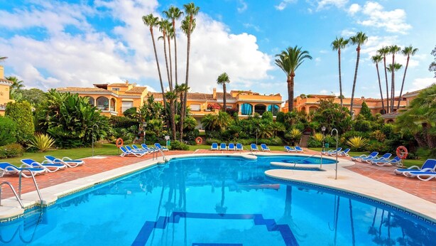 A swimming pool with blue water, surrounded by palm trees and lounge chairs. - Genteel Home Venalmar Terrace (Estepona)