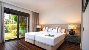 A double bed with a magazine, two bedside tables with lamps, a sliding glass door to a garden, and a wooden floor. - Genteel Home Venalmar Terrace (Estepona)