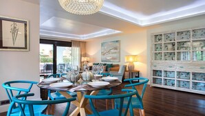 A dining area with a round table set for six, surrounded by blue chairs, a chandelier, and a view of the outdoors. - Genteel Home Venalmar Terrace (Estepona)