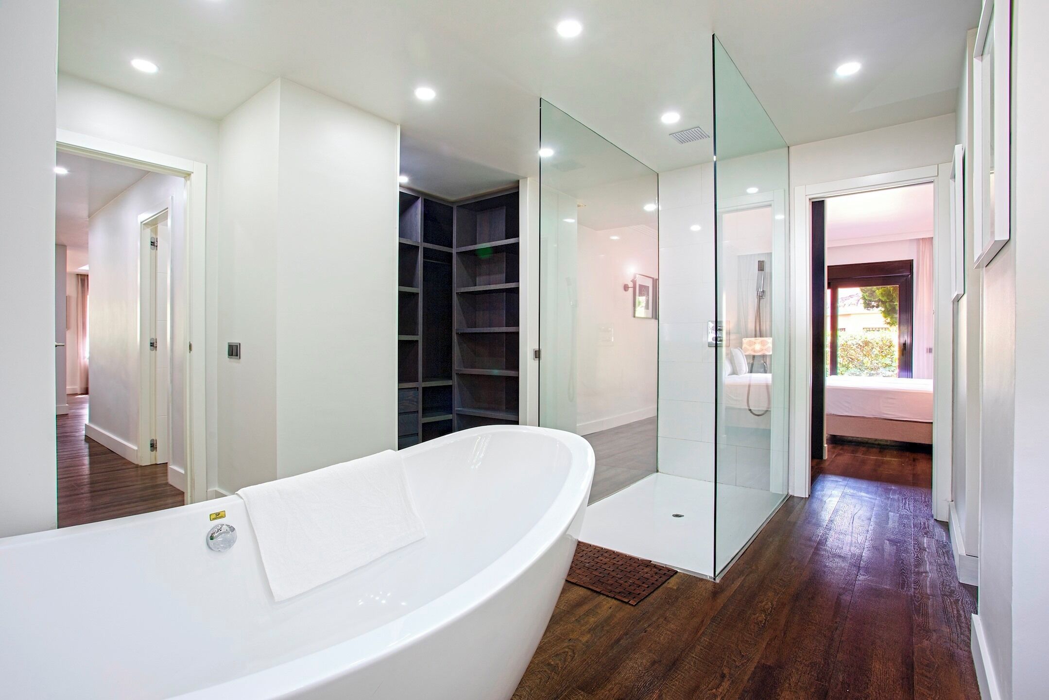 A modern bathroom with a freestanding bathtub, glass shower enclosure, and a visible walk-in closet.