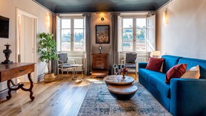 A cozy living room with a blue sofa, a wooden coffee table, a plant, and a view of the outdoors through large windows. - Genteel Home Piazza Pitti (Florence)