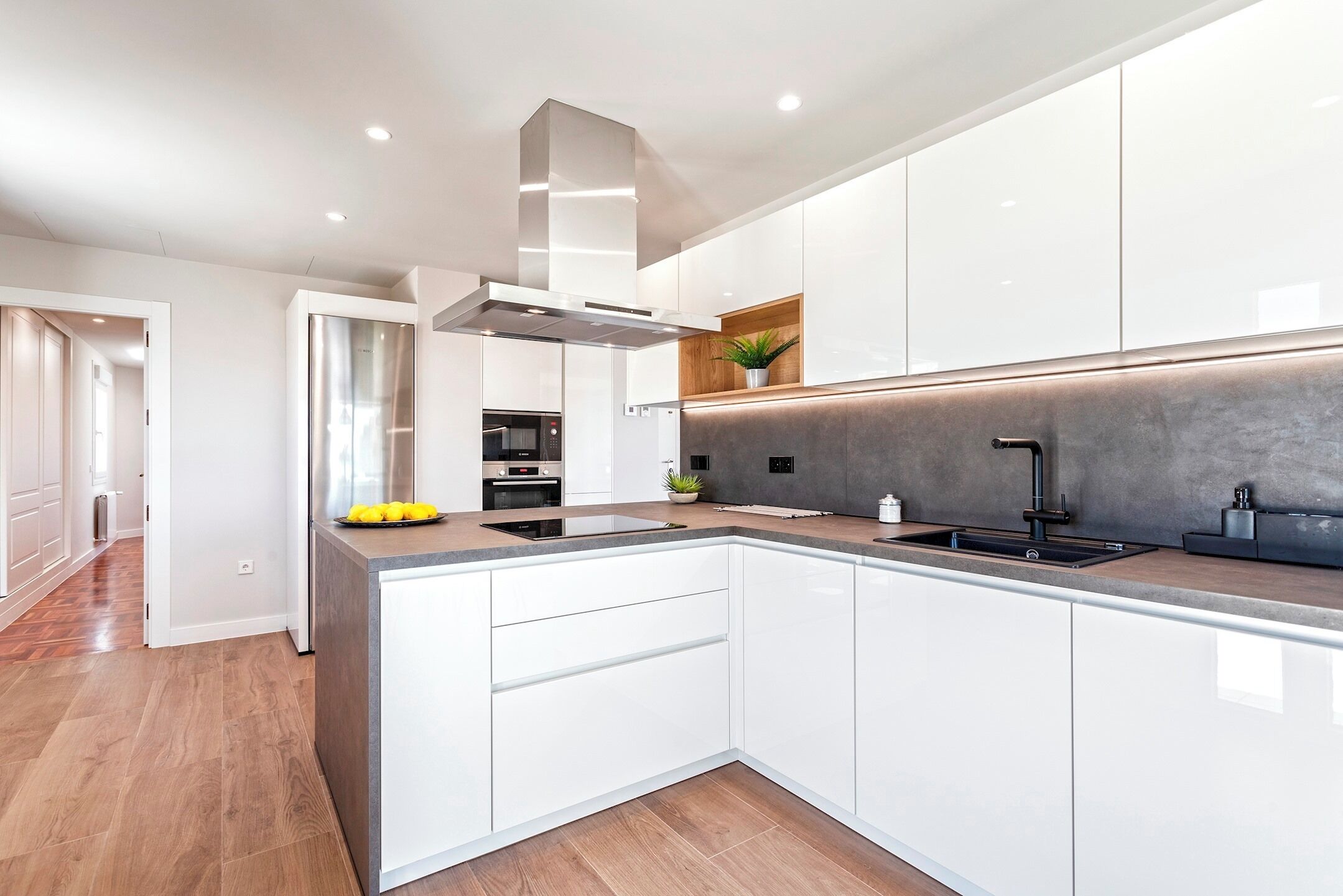 A modern kitchen with white cabinetry, a central island, and a built-in oven.