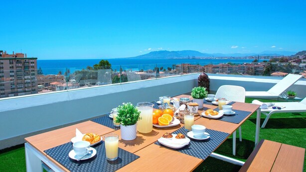 Un balcón con una mesa preparada para el desayuno, con vistas a una ciudad costera.