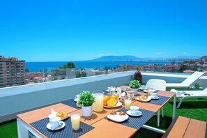 Un balcón con una mesa preparada para el desayuno, con vistas a una ciudad costera.