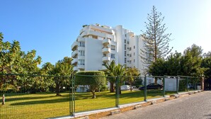 A multi-story residential building with balconies, surrounded by a green fence and trees. - Genteel Home Los Flamencos Terrace (Marbella)
