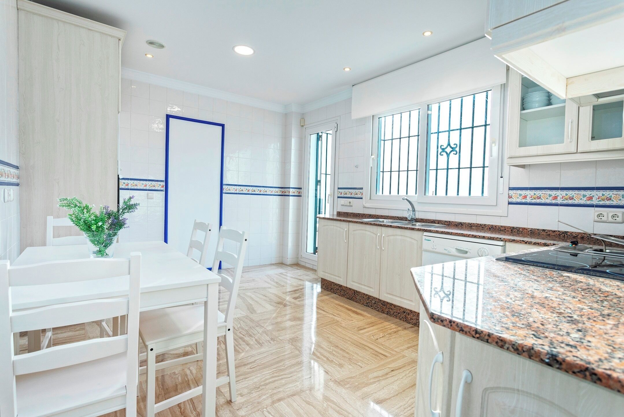 Una cocina moderna con armarios blancos, encimera de granito y una ventana con rejas.