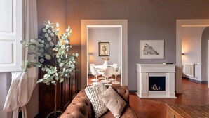 A living room with a brown sofa, a fireplace, a dining area with white chairs, and a large plant. - Genteel Home Biblioteca Nazionale (Florence)