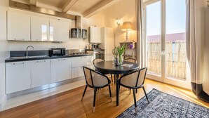 A modern kitchen with white cabinets, a dining area with a round table and chairs, and a large sliding glass door leading to a balcony. - Genteel Home Scarlatti (Florence)