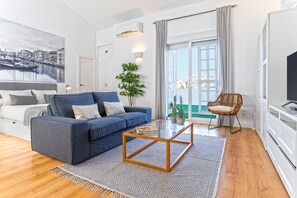 A modern living room with a blue sofa, a glass coffee table, a patterned rug, a wicker chair, and a large window with a view. - Genteel Home Castilla Terrace (Seville)