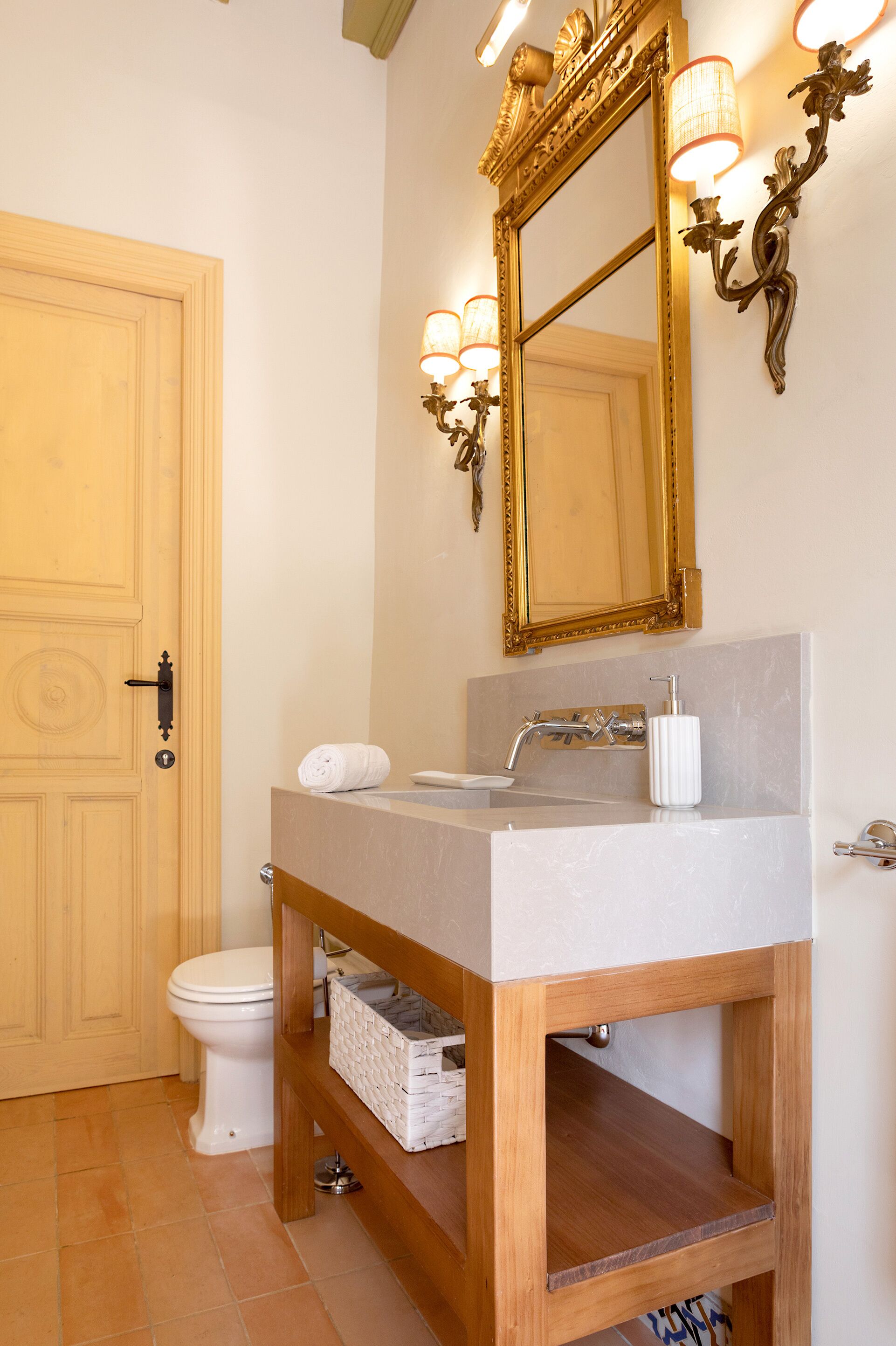 A bathroom with a wooden vanity, a white sink, a gold-framed mirror, and a toilet.