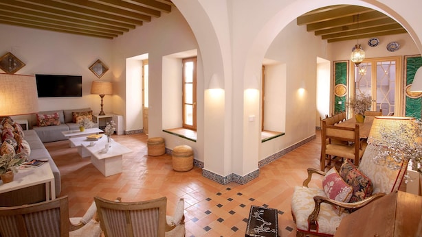 A spacious living area with a sofa, coffee table, and chairs. There is a television, a lamp, and a dining table with chairs. The room has a tiled floor and arches on the ceiling. - Genteel Home Pimienta (Seville)