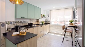 Een moderne keuken met lichte houten kastjes, een zwart aanrecht en een hangende lamp.