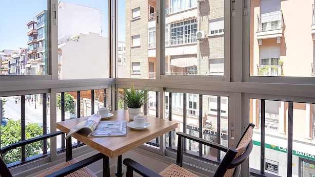 Een balkon met een tafel, stoelen, een bloempot en een krant.