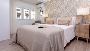Een slaapkamer met een groot bed, een nachtkastje met een lamp, een stoel en een wandairconditioner.