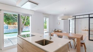 Et moderne køkken med en stor ø, et spiseområde med et træbord og udsigt til en swimmingpool.