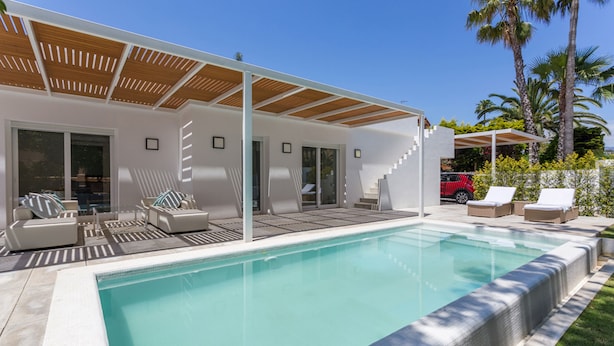 Et moderne poolområde med en overdækket terrasse, liggestole og en trappe til en anden overdækket terrasse.