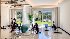 A modern gym with exercise equipment, large windows, and a view of greenery. - Genteel Home Prato (Prato)