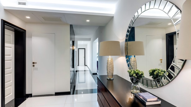 A modern hallway with a glossy white floor, a dark wooden bench, a round mirror, and two lamps. - Genteel Home Prato (Prato)