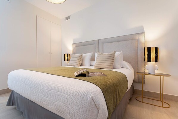 A modern bedroom with a large bed, a bedside table with a lamp, and a wardrobe.