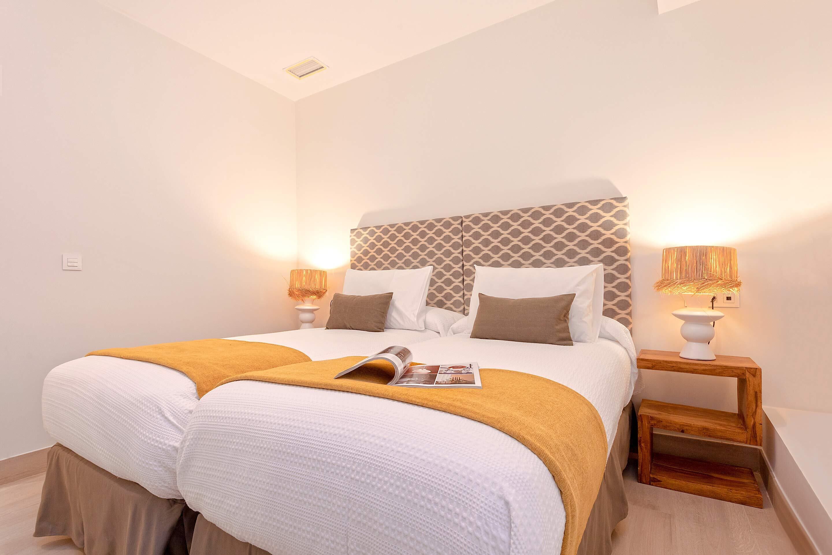 A neatly made bed with a magazine, two bedside lamps, and a wooden nightstand.