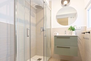 Un baño moderno con ducha envuelta en vidrio, un espejo redondo y un tocador minimalista con una planta.