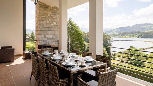 Comedor con una mesa dispuesta para seis personas, con vistas a un lago y colinas pintorescos.