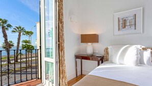 A hotel room with a bed, a nightstand, a lamp, a framed artwork, and a view of palm trees and a street through a glass door. - Genteel Home Paseo Marítimo (Málaga)