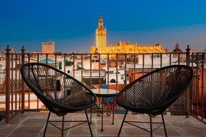 A balcony with two black wicker chairs and a small table, overlooking a cityscape with a prominent tower. - Genteel Home San Isidoro Terrace (Seville)
